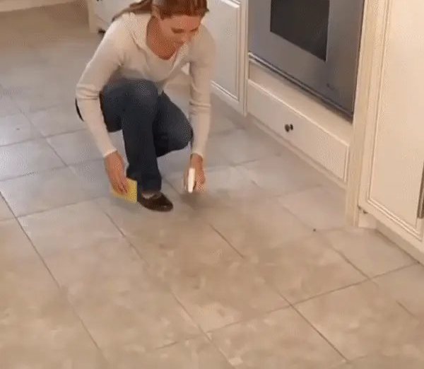 A woman kneeling to clean a tiled kitchen floor